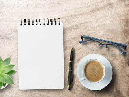 Blank notepad,glasses, pen and coffee cup on office desk background. Top view with copy space.