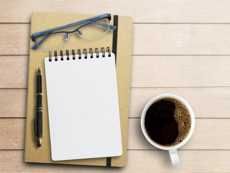 Blank notepad,glasses, pen and coffee cup on office desk background. Top view with copy space.