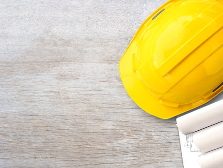 Yellow safety helmet or hard hat and construction paper plans on wood table background. Business...