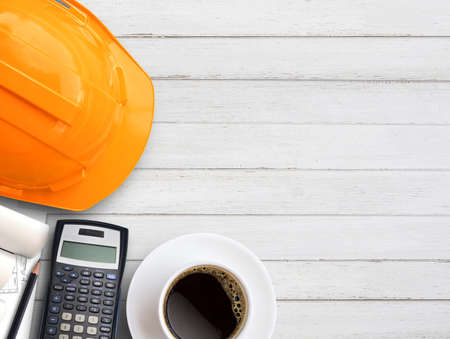 Orange safety helmet or hard hat,coffee,calculator and construction paper plans on wood table background. Business building idea, construction industry concept. Top view with copy space for your use.の写真素材