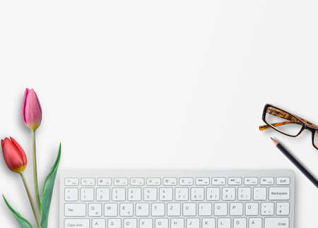 Top view with keyboard,glasses,pink tulip and pencil on white table background in office workplace.の写真素材