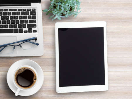 Top view blank tablet,glasses,notebook and cup of coffee on wood table background. copy space for your design.の写真素材