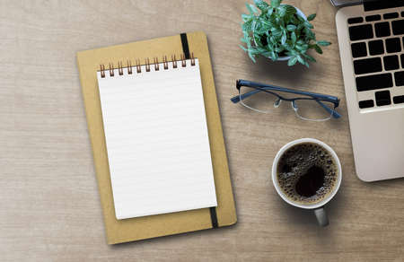Flat lay top view photo of laptop keyboard with mug of beverage green cactus and blank spiral copybook isolated brown loft backdrop with blank space for design.の写真素材