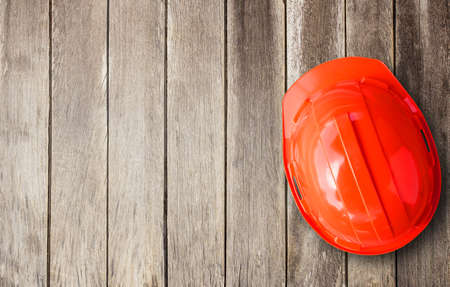 Red engineer safety helmet overhead view. Construction of brown wooden texture background space for designの写真素材