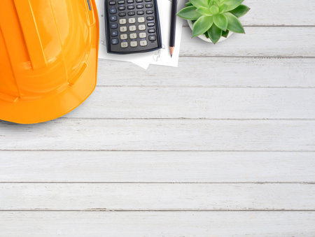 Orange safety helmet or hard hat,coffee,calculator and construction paper plans on wood table...