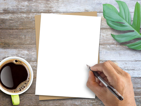 Office desk, Hand writing on blank white paper and fresh green leaves on wood table background. Top...