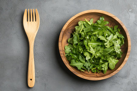 Fresh arugula salad in wooden bowl on grey background, top viewの写真素材