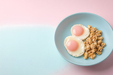 Fried eggs in a blue plate with granola on a pink backgroundの写真素材