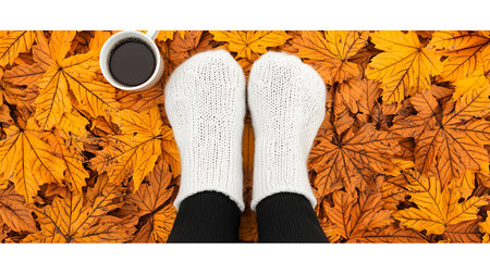 Female legs in woolen socks with cup of coffee on autumn leaves backgroundの写真素材
