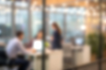 A modern office setting featuring a team collaborating around a table with laptops. Bright lighting and glass walls enhance the ambiance of focused teamwork.の写真素材