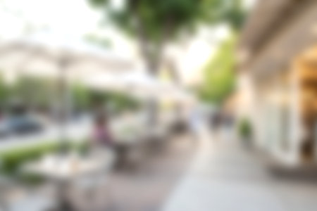A tranquil and blurred outdoor cafe scene featuring tables and umbrellas along a sidewalk, creating a warm and inviting atmosphere for diners in an urban setting.の写真素材