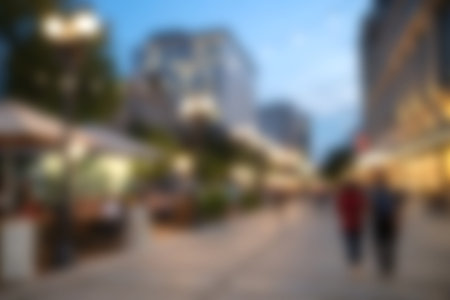 A picturesque urban street at dusk showcasing cafes with outdoor seating as a couple enjoys a leisurely stroll, highlighting city life and vibrant ambiance.の写真素材