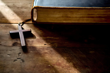An artistic composition depicting a wooden cross alongside an open Bible resting on a rustic wooden...