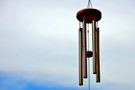 A serene wind chime gently sways in the breeze against a soft, overcast sky, creating a calming atmosphere. Ideal for nature-themed projects.の写真素材