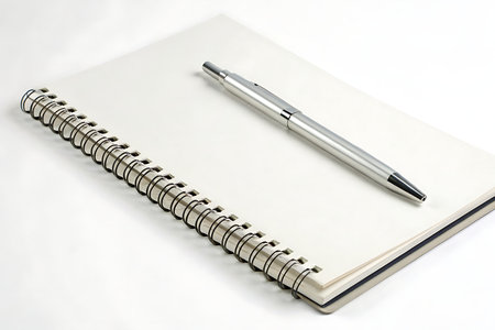 A silver pen rests on a blank spiral notebook, creating a perfect setting for jotting down ideas or sketches. Ideal for creative and organizational projects.の写真素材