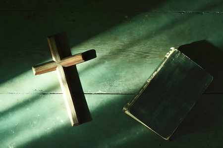 A wooden cross and an open book create a serene composition on a green surface, illuminated by...