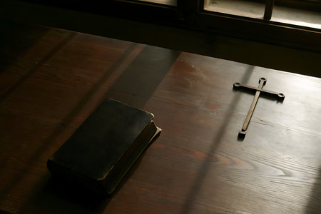 A serene wooden table featuring an open Bible and a simple cross, illuminated by natural light and subtle shadows, creating a tranquil atmosphere for reflection and devotion.の写真素材