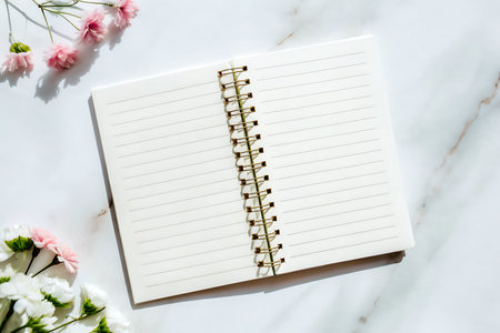 A clean blank notebook lies on a marble surface, surrounded by delicate flowers, ideal for planning...