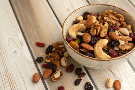 A vibrant bowl filled with a mix of nuts and dried fruits rests on a rustic wooden surface. Perfect...