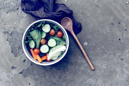 This image features a vibrant salad composed of fresh vegetables such as lettuce, cucumber, and tomatoes. A wooden spoon adds a cozy touch. Perfect for healthy dining.の写真素材