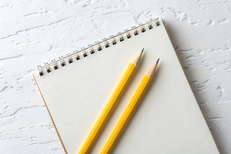 A blank notebook lies on a table accompanied by two yellow pencils, perfect for sketching or...