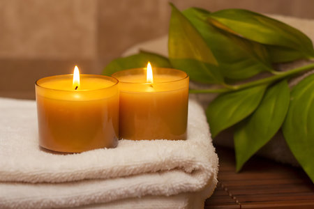 A calming spa scene featuring two glowing candles on soft towels, complemented by lush greenery, perfect for relaxation and self-care moments.の写真素材