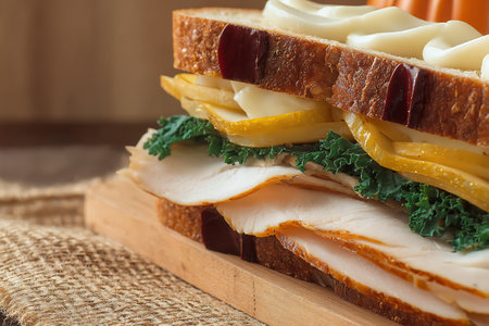 A tempting turkey sandwich layered with fresh vegetables and a creamy spread, displayed on a rustic wooden surface, ideal for meal inspiration.の写真素材