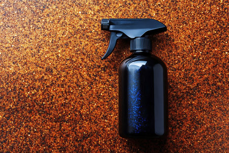 A sleek black spray bottle sits atop a shimmering brown surface. Ideal for showcasing household cleaning products or minimalist design aesthetics.の写真素材