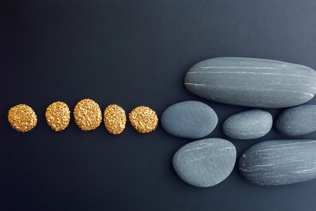 A serene composition of golden round objects contrasted with smooth pebbles on a dark background,...