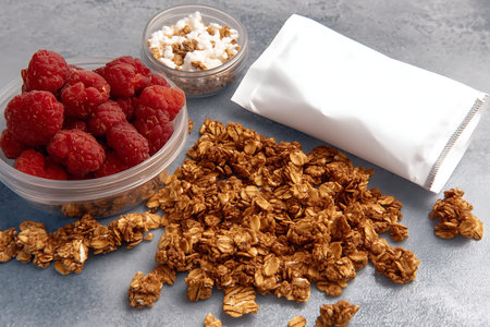 A vibrant display of healthy ingredients including granola, fresh raspberries, and a white package,...