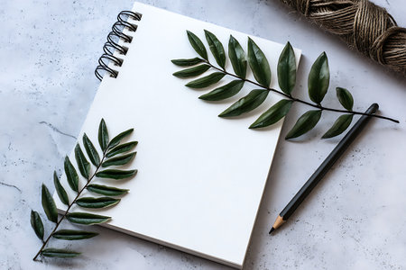 Aesthetically pleasing flat lay of a blank sketchbook, fresh green leaves, and a black pencil arranged on a marble surface, perfect for creative inspiration.の写真素材