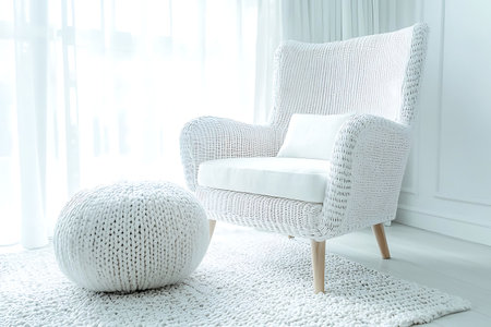 A stylish white woven chair paired with a soft cushion and a knitted pouf enhances any bright room's decor. Ideal for modern and cozy interiors.の写真素材