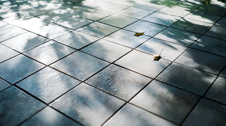 A serene outdoor setting featuring a clean tiled floor lightly adorned with fallen leaves. Sunlight creates soft shadows, enhancing the tranquil atmosphere.の写真素材