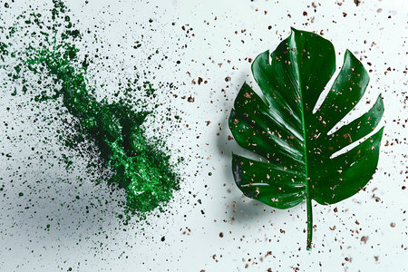 A striking image featuring a large green leaf and vibrant splashes of glitter on a white backdrop,...