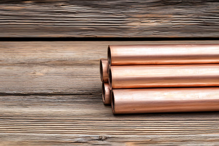 A close-up view of stacked copper pipes on a rustic wooden surface. Ideal for construction, DIY, and plumbing projects or showcasing industrial materials.の写真素材