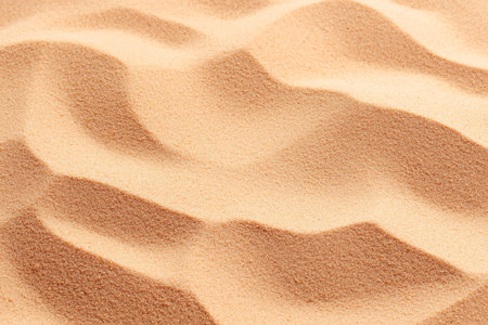 A close-up view of fine golden sand showcasing gentle undulating patterns. Perfect for backgrounds,...