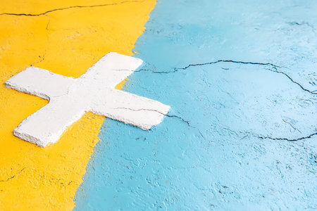 This image features a colorful abstract background with a striking contrast of yellow and blue textures and a prominent white cross symbol, ideal for creative projects.の写真素材
