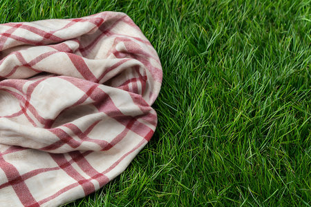 A cozy checkered blanket rests gently on fresh green grass, creating an inviting setting ideal for outdoor picnics or relaxation. The scene captures comfort and warmth amidst nature.の写真素材