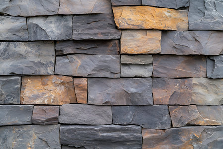 A detailed view of a natural stone wall featuring various shades of gray and brown. This image...