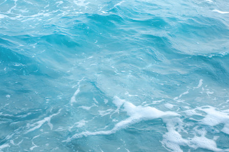 This image showcases a serene and calm ocean water surface, featuring gentle waves and soft foam....