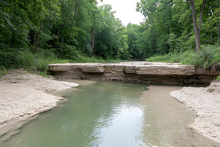 This image showcases a serene natural landscape featuring a calm river bordered by sandy shores and...