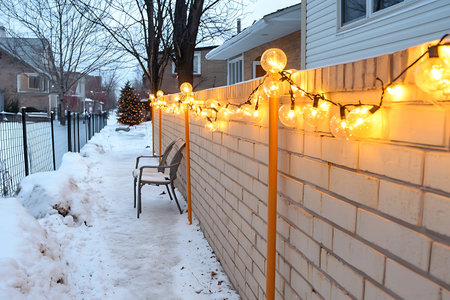 A serene winter scene featuring a snow-covered pathway lined with warm glow lights, inviting chairs,...