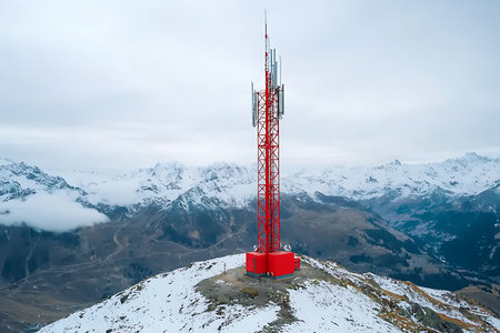 A striking red communications tower stands firmly on a snow-covered mountain peak, surrounded by breathtaking snowy landscapes and distant mountain ranges.の写真素材