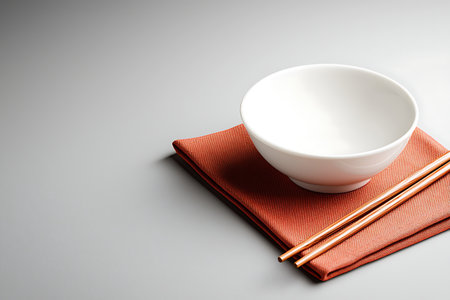 A minimalist composition featuring an elegant white bowl and wooden chopsticks resting on a stylish red cloth. Ideal for dining and culinary themes.の写真素材