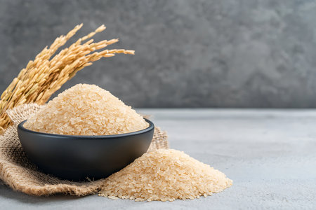 This image features a heap of uncooked rice grains in a black bowl, accompanied by rice stalks. Perfect for culinary and agricultural themes.の写真素材