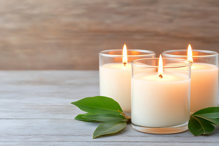 This serene image features three burning candles in glass holders, beautifully complemented by green leaves on a wooden surface, creating a tranquil atmosphere.の写真素材