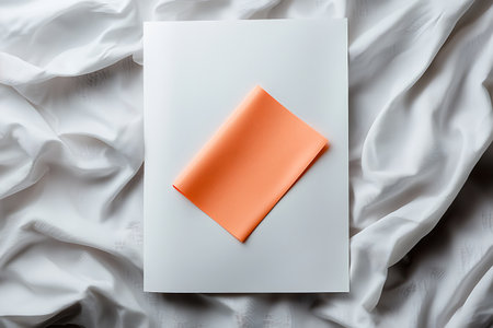 This image showcases a vibrant orange cloth elegantly placed on a white background, complemented by soft, draped fabric, ideal for artistic projects and modern design themes.の写真素材