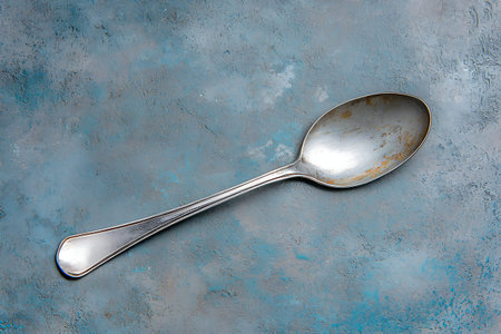 A vintage silver spoon resting on a textured blue background, creating a rustic and artistic feel. Ideal for kitchen and dining themes.の写真素材