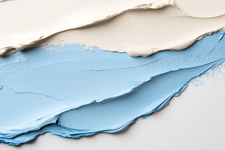 Close-up view of textured cream and light blue acrylic paints layered on a canvas, showcasing rich...