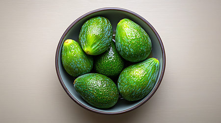 A close-up view of fresh green avocados beautifully arranged in a bowl against a soft textured...